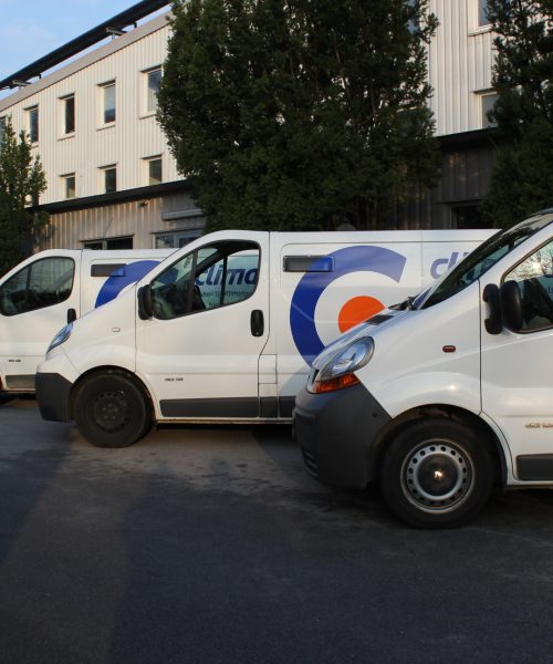 Drei weiße Firmen-Kastenwagen des Unternehmens „climatic“ stehen schräg hintereinander auf einem Parkplatz aufgereiht. Im Hintergrund sind ein mehrstöckiges Firmengebäude sowie grüne Bäume zu sehen.
